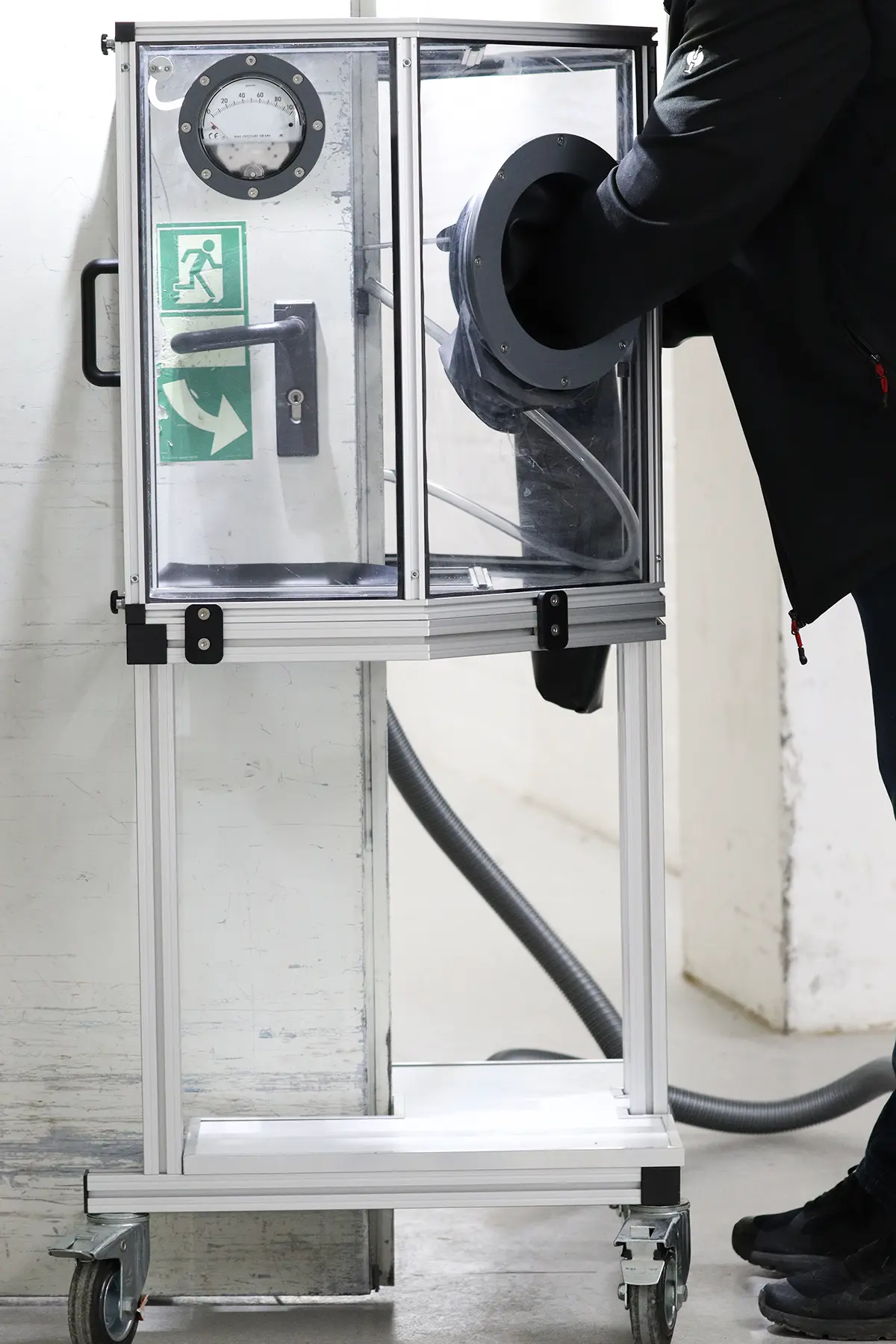 An einer Tür befindet sich ein Glaskasten, der die Schließeinrichtung der Tür komplett bedeckt. In diesen Glaskasten steckt ein Mitarbeiter seine Arme um die Schließeinrichtung zu warten, zu kontrollieren oder zu wechseln.