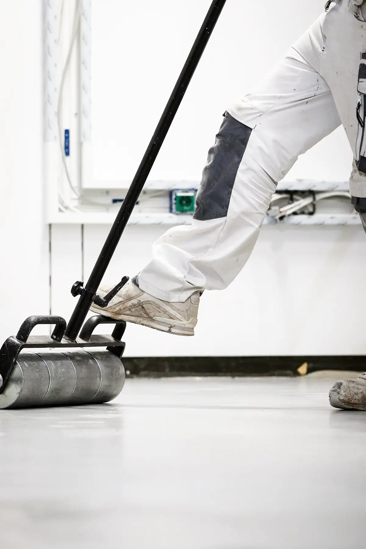 Der Fuß eines Handwerkers befindet sich auf der Andrückwalze um den neuen PVC Boden anzudrücken.