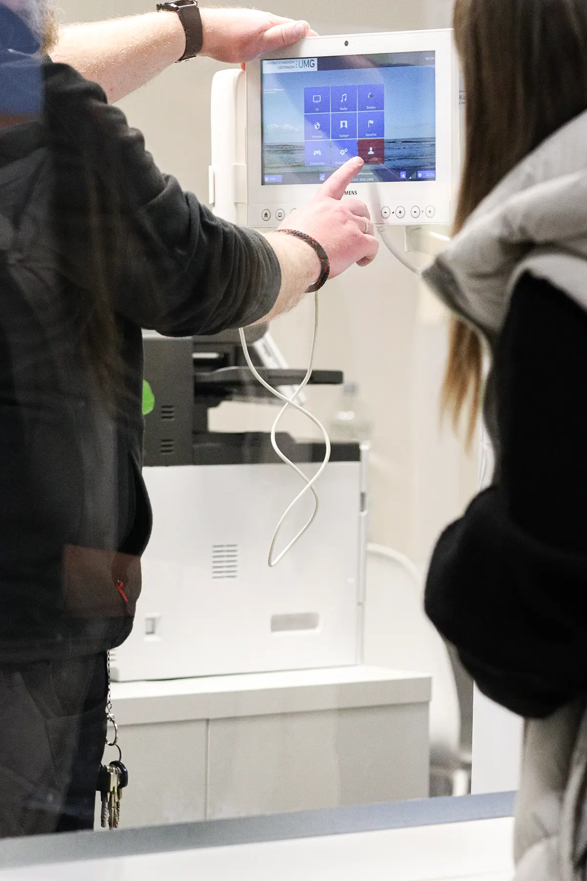 Ein Mitarbeiter zeigt einer anderen Person die Funktionsweise des internen Patientenentertainmentsystems.
