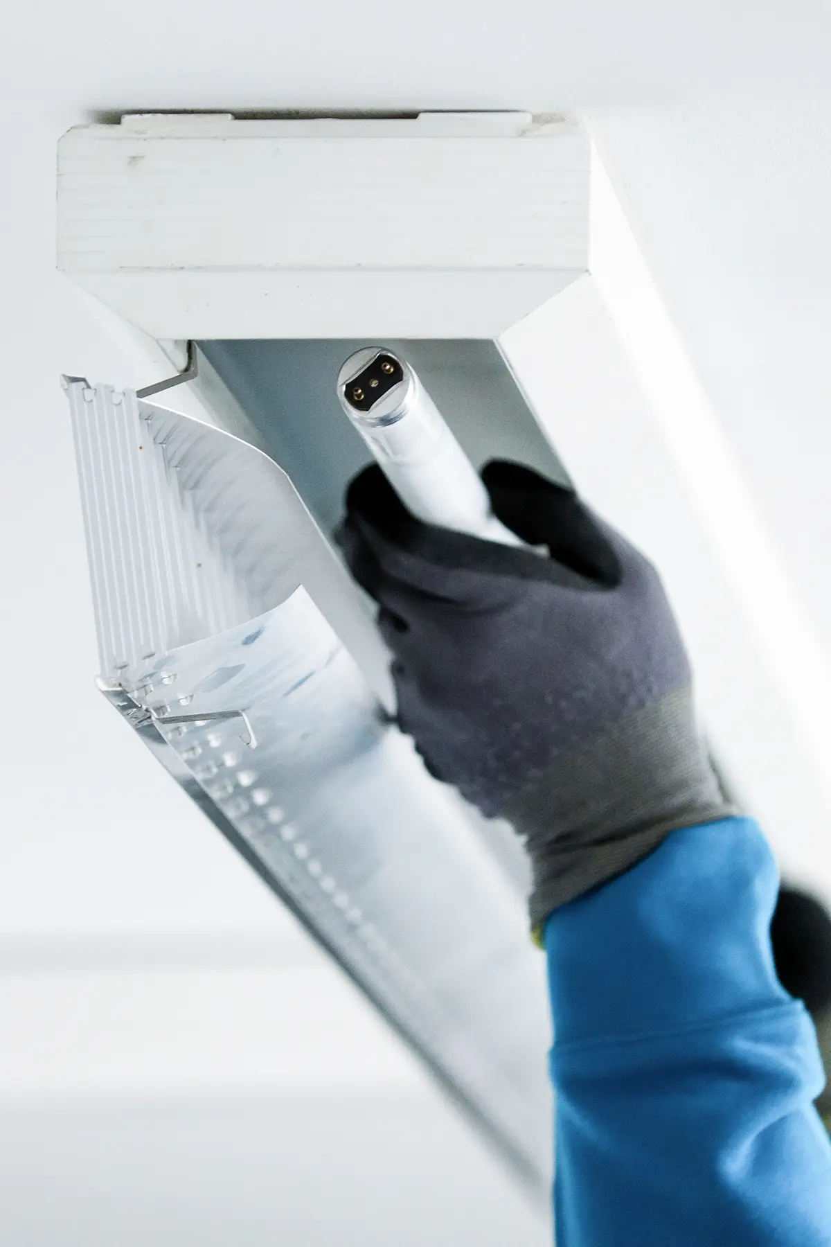 Ein Bauarbeiter wechselt die Neonröhre einer Lampe. Er hat Handschuhe an und hält die Neonröhre in der Hand, um sie in einer Lampe zu befestigen.