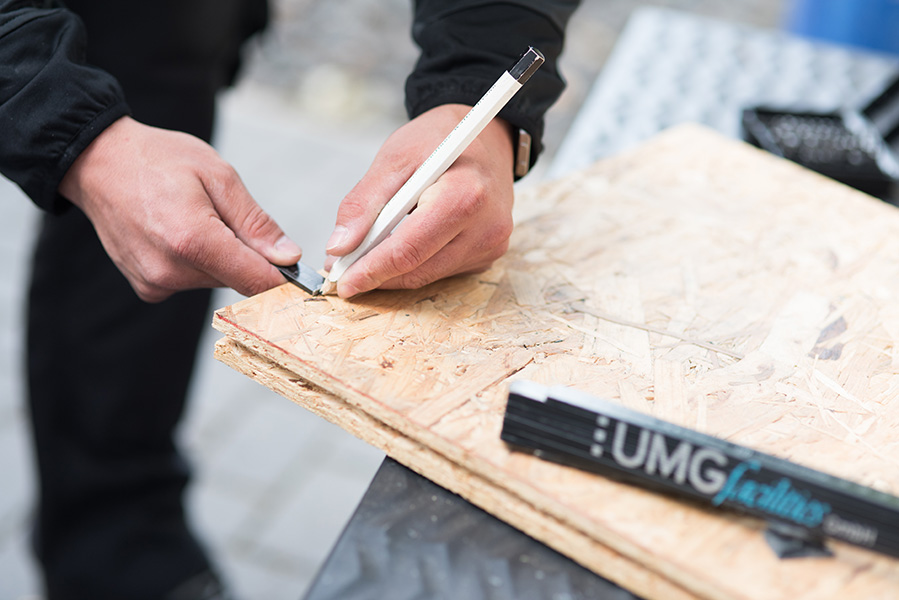 Ein Mitarbeiter zeichnet mit einem Bleistift Maße auf einer OSB Platte.
