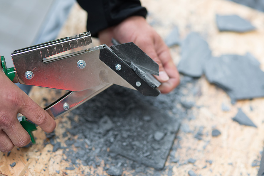 Ein Mitarbeiter schneidet Schieferplatten mit einer Schieferschere.