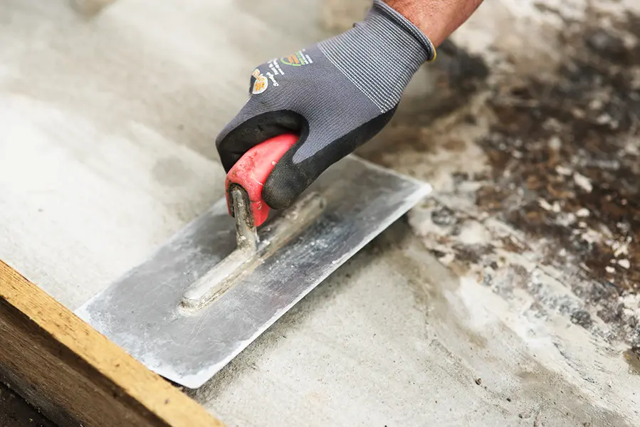 Ein Bauarbeiter streicht den Beton eines Fundamentes glatt. Dazu benutzt er eine Maurerkelle um den Beton abzustreichen. Zudem trägt er einen Handschuh.