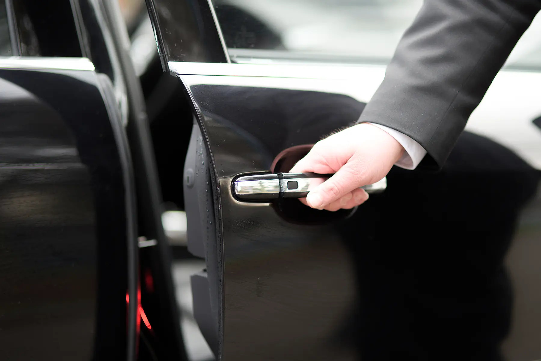 Ein freundlicher Mitarbeiter in Dienstkleidung öffnet die Tür eines Autos für einen Fahrgast. Der Service vermittelt einen professionellen und hilfsbereiten Eindruck.