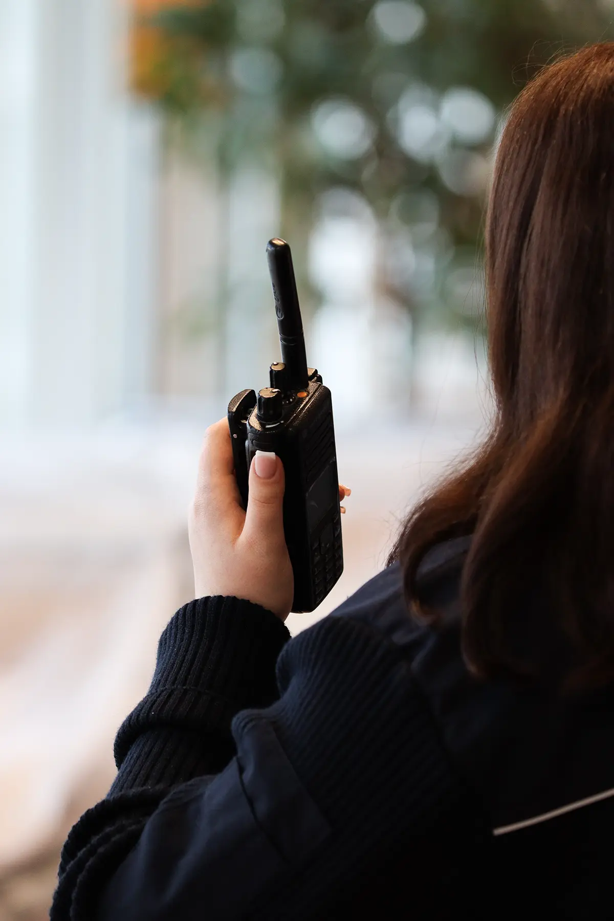 Eine Silhouette einer Mitarbeiterin im Sicherheitsdienst. Sie hat braune Haare und hält in der linken Hand ein Funkgerät. Es scheint, als würde sie einen Funkspruch abgeben.