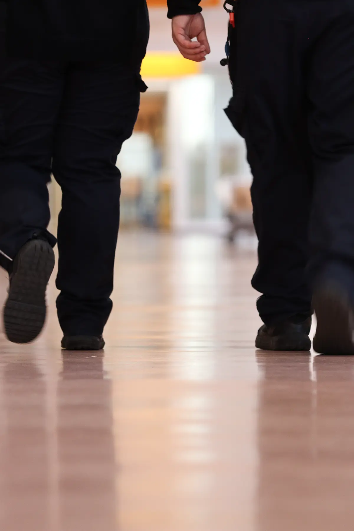 Zwei Mitarbeitende im Sicherheitsdienst bestreifen einen Flur. Zu sehen sind die Beine der beiden Mitarbeitenden, da sie zusammen die Bestreifung durchführen.