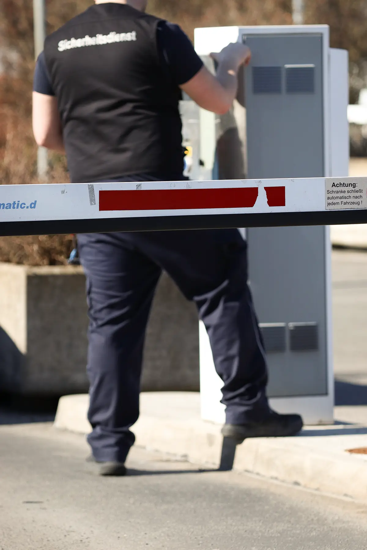 Eine Schrankenanlage für einen Parkplatz, die von einem Mitarbeiter des Sicherheitsdienstes bedient wird. Der Mitarbeiter steht an einem Schrankenterminal und wird von dem Mitarbeiter bedient.